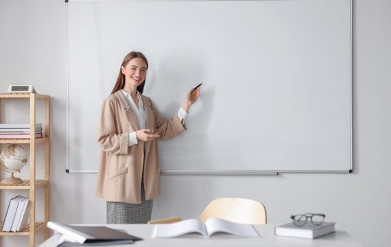 Happy,Young,Teacher,Explaining,Something,At,Whiteboard,In,Classroom.,Space